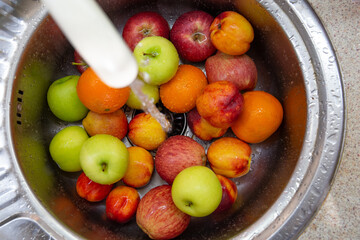 Many different colored fruits: oranges, apples, nectarines in the kitchen sink under running water
