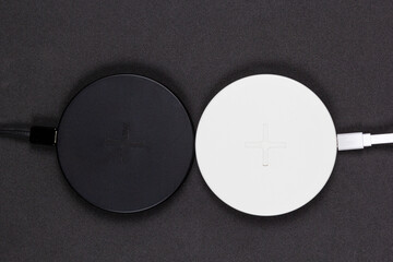 Two round black and white wireless chargers for phone on black background.
