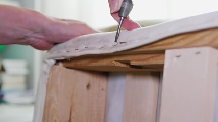 A woman with a screwdriver pulls out metal staples from the mattress for repair.