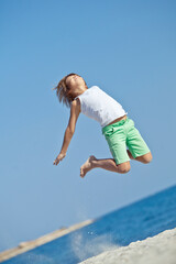 Obraz premium Child playing on ocean beach. Kid jumping in the waves. Sea vacation for family with kids. Little boy running on tropical beach of exotic island during summer holiday. High quality photo.