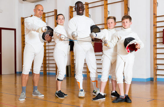 Portrait of smiling mixed age group of athletes with foils at fencing workout