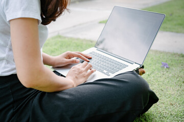 Naklejka premium Beautiful Woman Relaxing and Using Laptop While Sitting on Grass Field, Asian Woman Working Online on Laptop Device and Joying .Social Media. Relaxation Leisure Activities Lifestyles/Work at Home