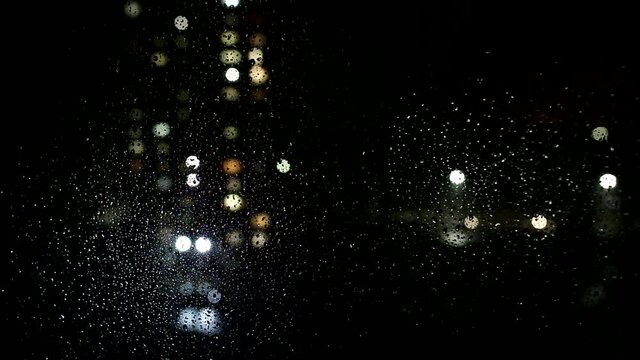 Raindrops on the glass of the window, outside the window the street driving cars, bad weather. Background, copy space for text, night