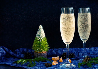a pair of misted glasses of champagne wine among christmas decor, dark blue shining background, copy space