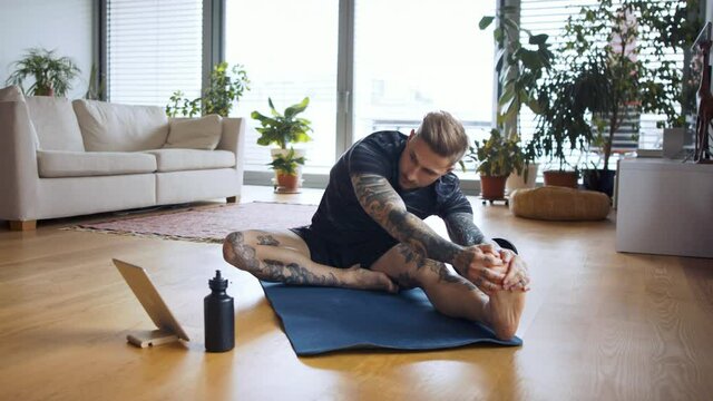 Front view portrait of man with tablet doing workout exercise indoors at home.