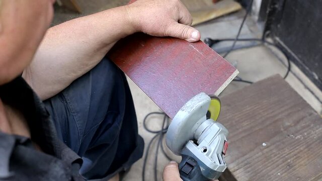 A man protects a wooden panel with a grinding wheel and a grinder. Manufacturing of furniture for a summer residence, hobby