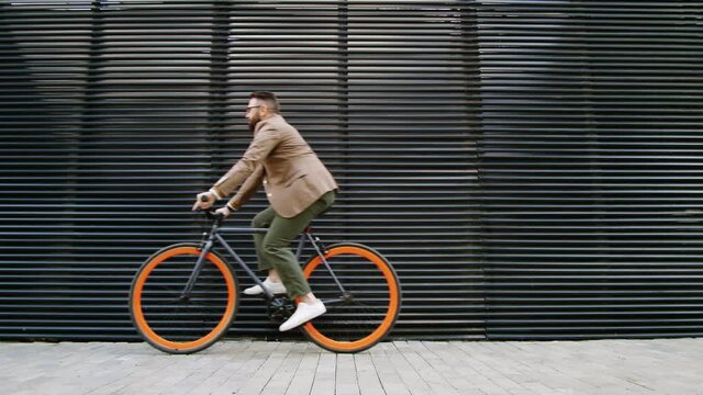 Side view shot of young Caucasian businessman riding bike along urban street in the city while going to work in the morning