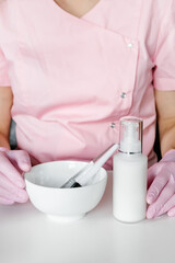 Cosmetic brushes in white bowl in woman's hands. Cosmetologist in pink uniform and gloves holding skin care products. 