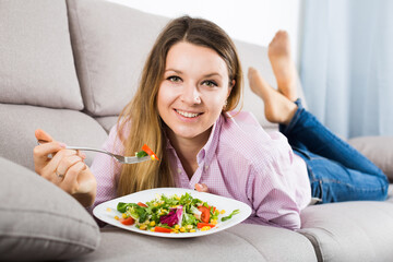 Obraz na płótnie Canvas Young smiling woman enjoying tasty green salad at home