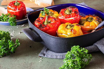 Baked stuffed sweet bell peppers with chicken or turkey, corn and herbs in deep dish, green concrete background.