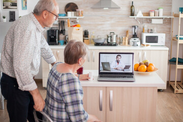 Senior couple during online medical check up from their home. Video conference with doctor using laptop in kitchen. Online health consultation for elderly people drugs ilness advice on symptoms