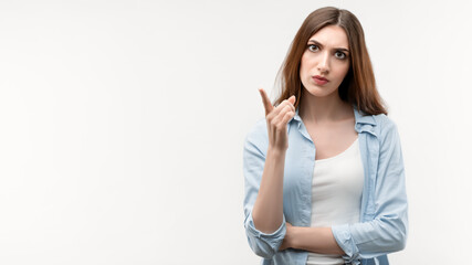 Serious young woman raises index finger, says Attention please. Studio shot, white background. Facial expression concept