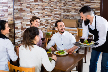 Smiling male waiter carrying order for visitors in country restaurant