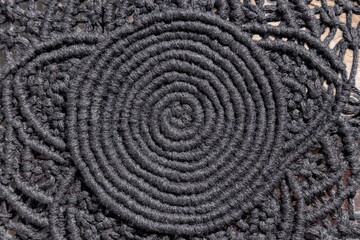Fragment of a macrame product made of black rope with a spiral in the center and a circular lace pattern, top view