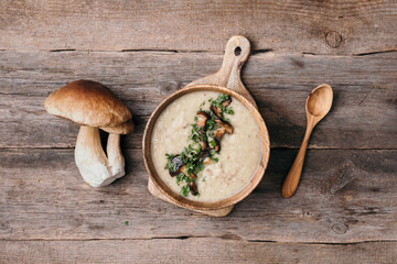 Wooden bowl of cream mushroom soup with fried mushrooms, vegetables, spices, raw boletus edulis...