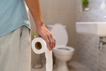 Man holding toilet paper roll in bathroom. Man suffers from diarrhea. Diarrhea concept.