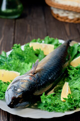 Fresh mackerel fish on a platter with lettuce and lemon wedges, ingredients for cooking fish. Close-up with shallow depth of field on fresh mackerel. Dark wood background