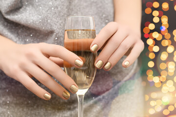 Female hands with gold nail design. Gold glitter nail polish manicure. Woman hold champagne glass