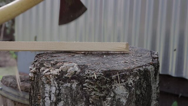 A close-up ax chops a stick on a birch stump. Procurement of firewood from woodworking waste. In the background is a corrugated sheet metal wall. Warm summer day. Side view. Soft light.