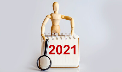 Wooden man shows with a hand to white notepad with text 2021