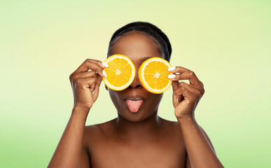 beauty, skin care and detox concept - beautiful african american woman making eye mask of oranges over lime green natural background