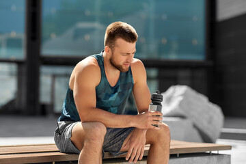fitness, sport and people concept - tired young man with bottle of water sitting on city bench © Syda Productions