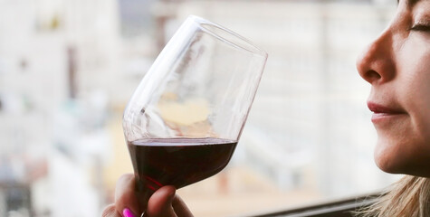 Happy moment of  woman standing in her apartment sipping a glass of red wine with her eyes closed in pleasure, side view