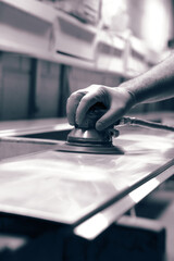 Man using orbital sander to prepare a metal panel.  With colour toning