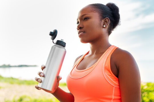 Fitness, Sport And Healthy Lifestyle Concept - Young African American Woman Drinking Water From Bottle Outdoors