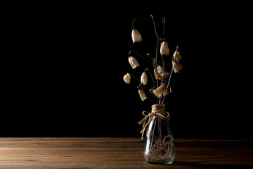 glass vase with dried flowers on wooden table on black background