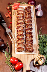 Lula kebab fried on charcoal with vegetables and spices on a wooden board.