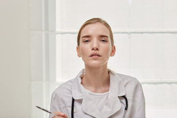 A young female doctor in a medical gown looks at the camera and says. In the hands of a writing pen. White background. Doctor's advice.