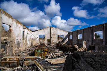 Interior de almacén industrial con tejado derruido y cielo lleno de nubes