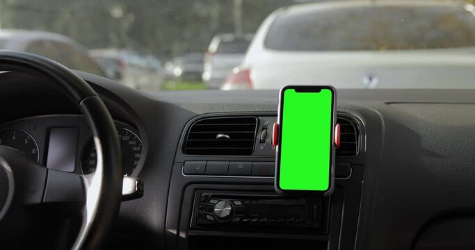 Mid shot of the iPhone 11 Pro Max placed on the car dashboard. A device with a keyed green screen. Autumn fall street, traffic jam. Blank mock-up screen. 