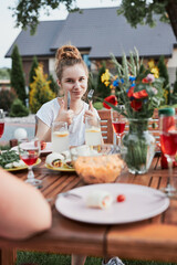 Young woman having a meal from grill during summer family picnic outdoor dinner in a home garden. Girl enjoying her tasty meal showing okay gesture. Close up of table with food and dishes