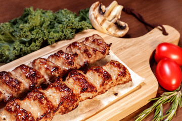 Lula kebab fried on charcoal with vegetables and spices on a wooden board.