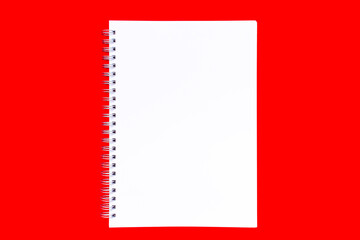 Concept of the New year, Christmas or Valentine day. Blank white notebook sheet with a spiral on a plain red background. Layout, flat lay or mockup. Copy space, place for text.