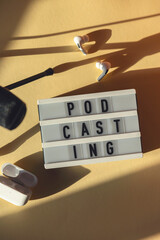 Naklejka premium Podcasting lettering next to microphone and wireless headphones at workplace in hard shadows