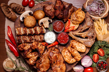 Meat platter fried on charcoal with spices on a wooden board. Rack of lamb, pork, lamb, kebab, chicken, mushrooms and tomato sauces for meat.