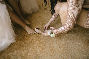 bridesmaid helps the bride to put on wedding shoes