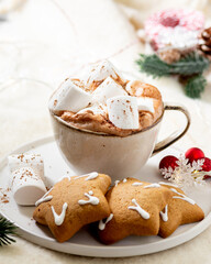 Hot cocoa or hot chocolate with marshmallows in a ceramic Cup surrounded by gingerbread, Christmas tree branches and ornaments on a brown wooden table. Christmas or new year's composition