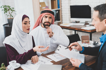  Arab couple sits at a table with a realtor.