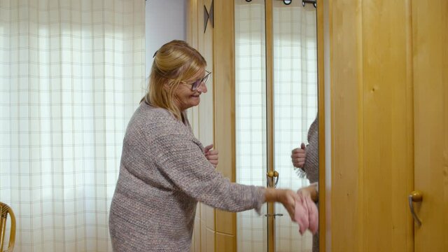 Older woman cleaing the mirror in the bedroom of her house in the afternoon