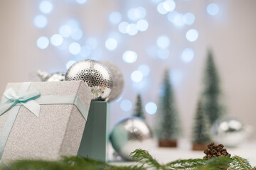silver Christmas balls in a gift box on a background of Christmas trees and blue bokeh