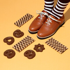 Leg in vintage striped socks and shoes in stylish isometric sweet cookies space. Minimal still life fashion food art. Chocolate lover. Holidays party time, winter christmas mood season