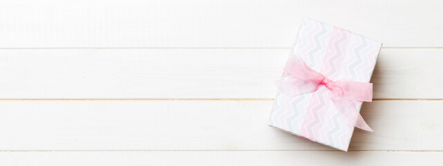 Beautiful gift box with a colored bow on the white wooden table. Top view banner with copy space for you design