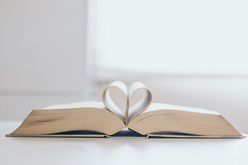 open book on white wooden table with pages forming a heart