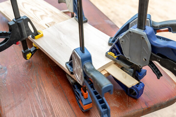 Joining wooden handmade box with clamps joiners after glueing. Different chisels, drills and pencils at craftsman workshop. DIY instruments on wood workbench. Workplace organization arrangement