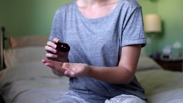 Woman Sitting On Bed Wearing Pyjamas Taking Medication