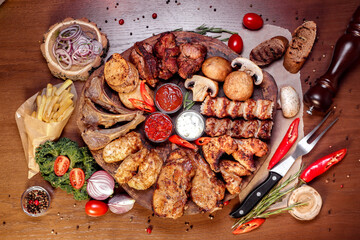 Meat platter fried on charcoal with spices on a wooden board. Rack of lamb, pork, lamb, kebab, chicken, mushrooms and tomato sauces for meat.